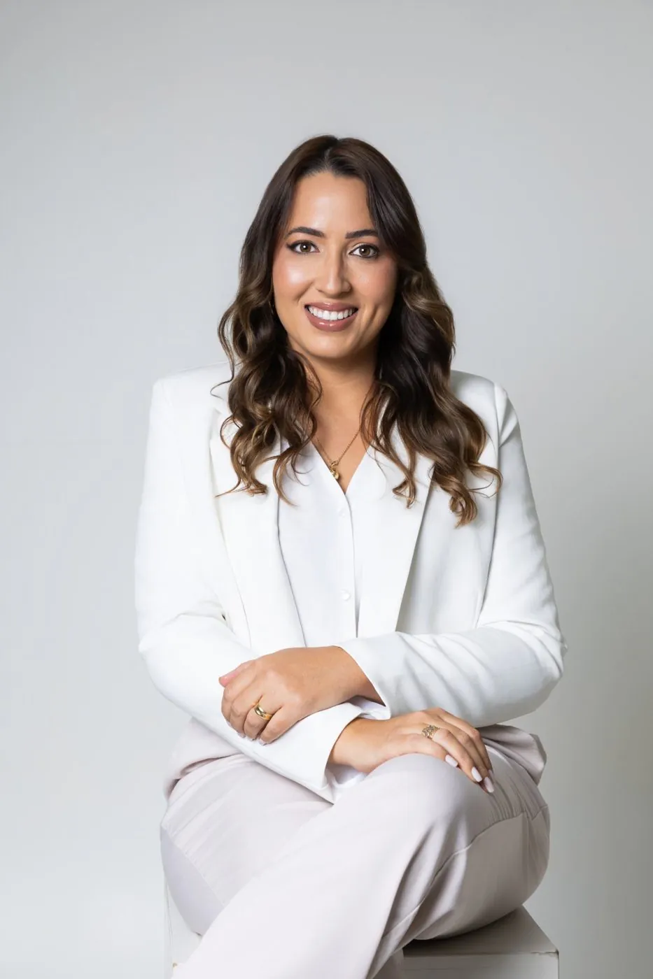 Bruna Câmara, de terno branco, sentada e sorrindo