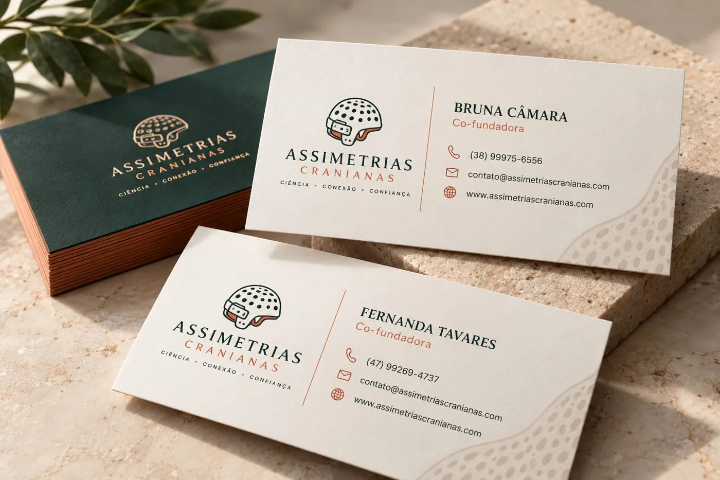 Cartões de visita de Bruna Câmara e Fernanda Tavares com a marca Assimetrias Cranianas sobre pedra clara